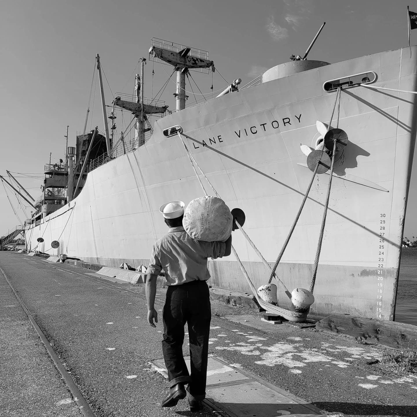 Photo of sailor walking on dock toward SS Lane Victory
